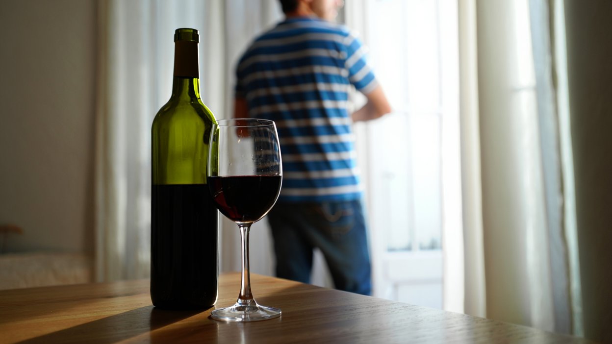 мужчина смотрит в окно, за ним стоит вино на столе